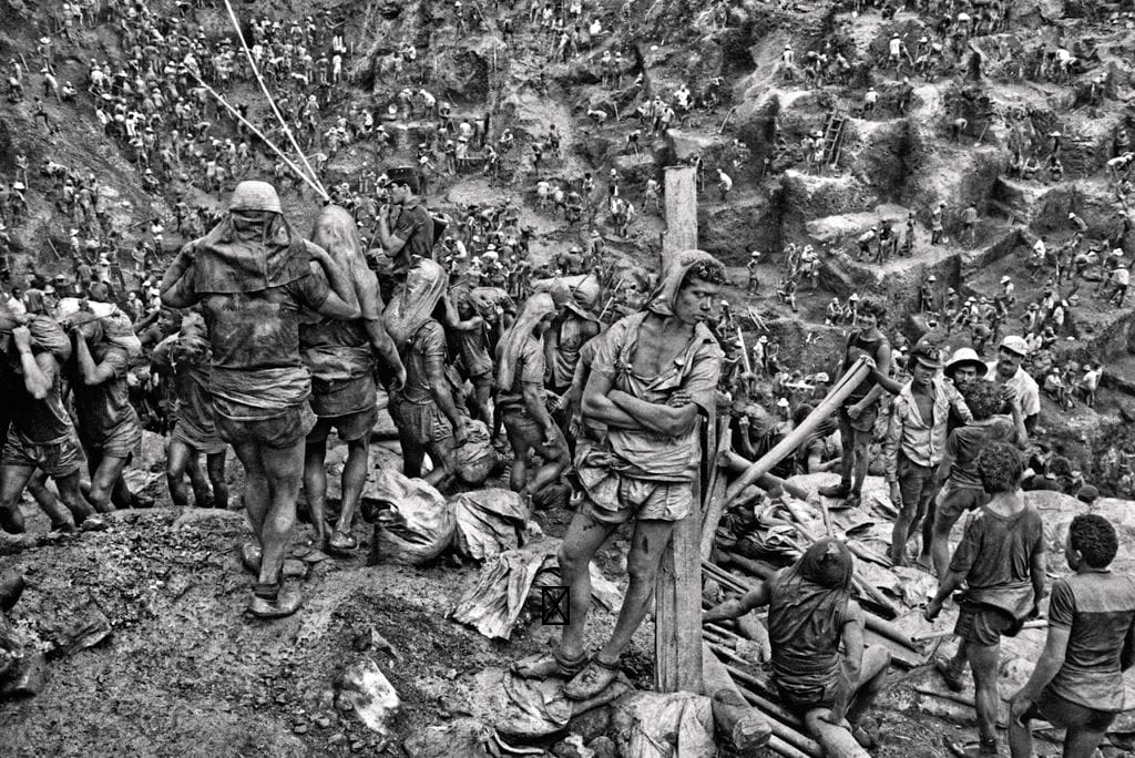 A black-and-white photograph. A goldmine in South America. Thousands of workers tiling.